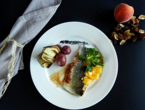 Spigola con riduzione al bellini, insalata di songino e pesche, patate magenta al vapore e chips di melanzane