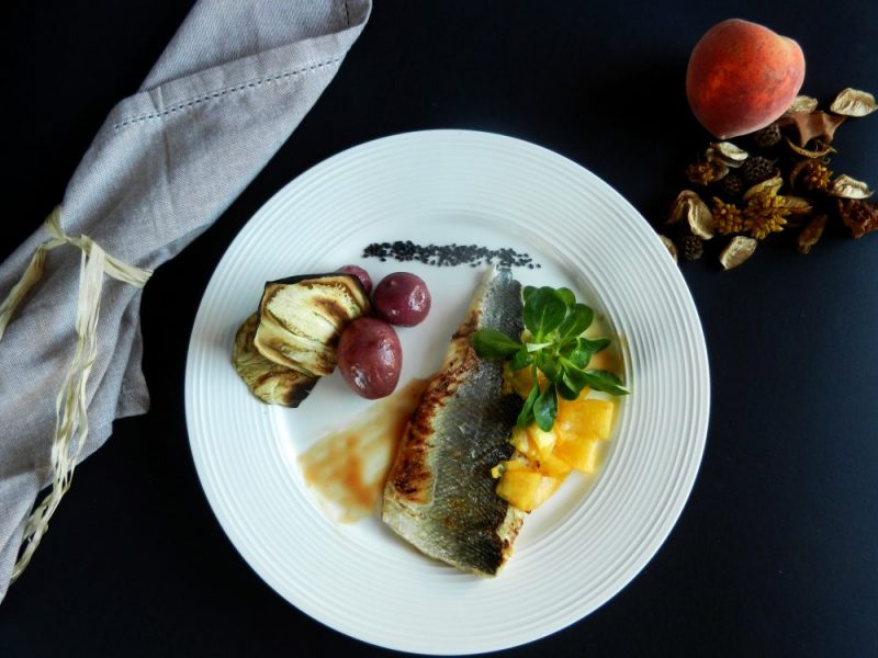 Spigola con riduzione al bellini, insalata di songino e pesche, patate magenta al vapore e chips di melanzane